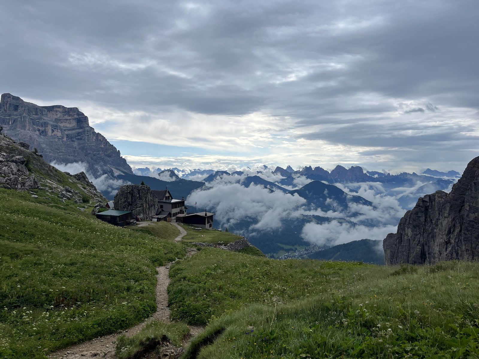 A rifugio and alpine path above clouds in a dramatic Dolomite valley.