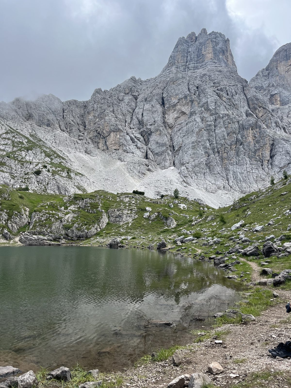 Cold alpine lake below grey Dolomite cliffs in July.