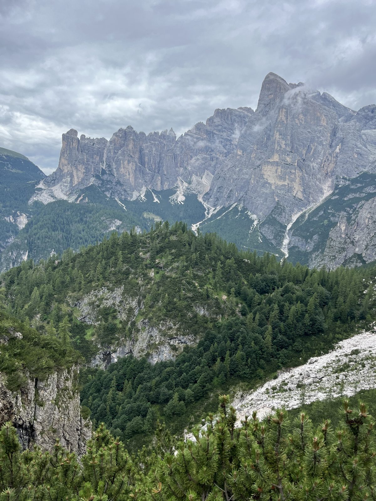 Storm clouds over steep Dolomite cliffs and forested slopes.